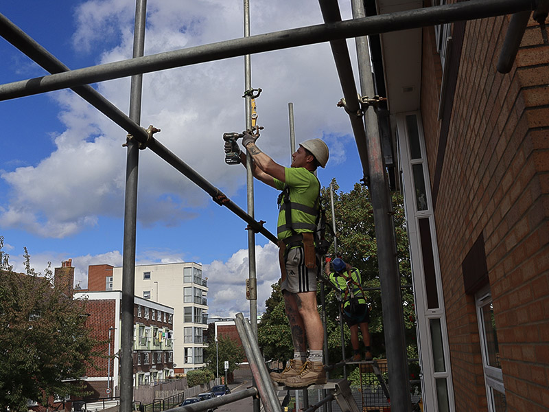 A BSL scaffolder fixing tube overhead with a second operative behind