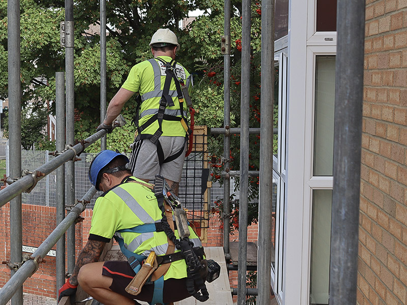 Two BSL scaffolders handling tube on a boarded lift