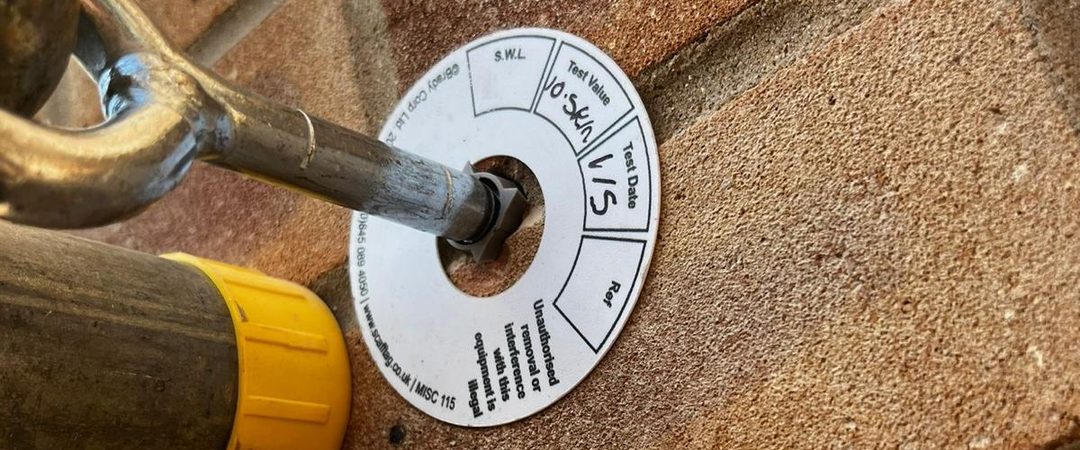 A tested scaffold tie anchored into brickwork, with its tie tag recording the test value and test date